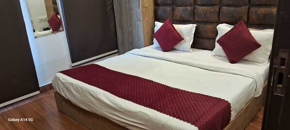 A bed with white bedding and red pillows, a wooden headboard, and a red blanket. - Hotel Trueman (Amritsar)