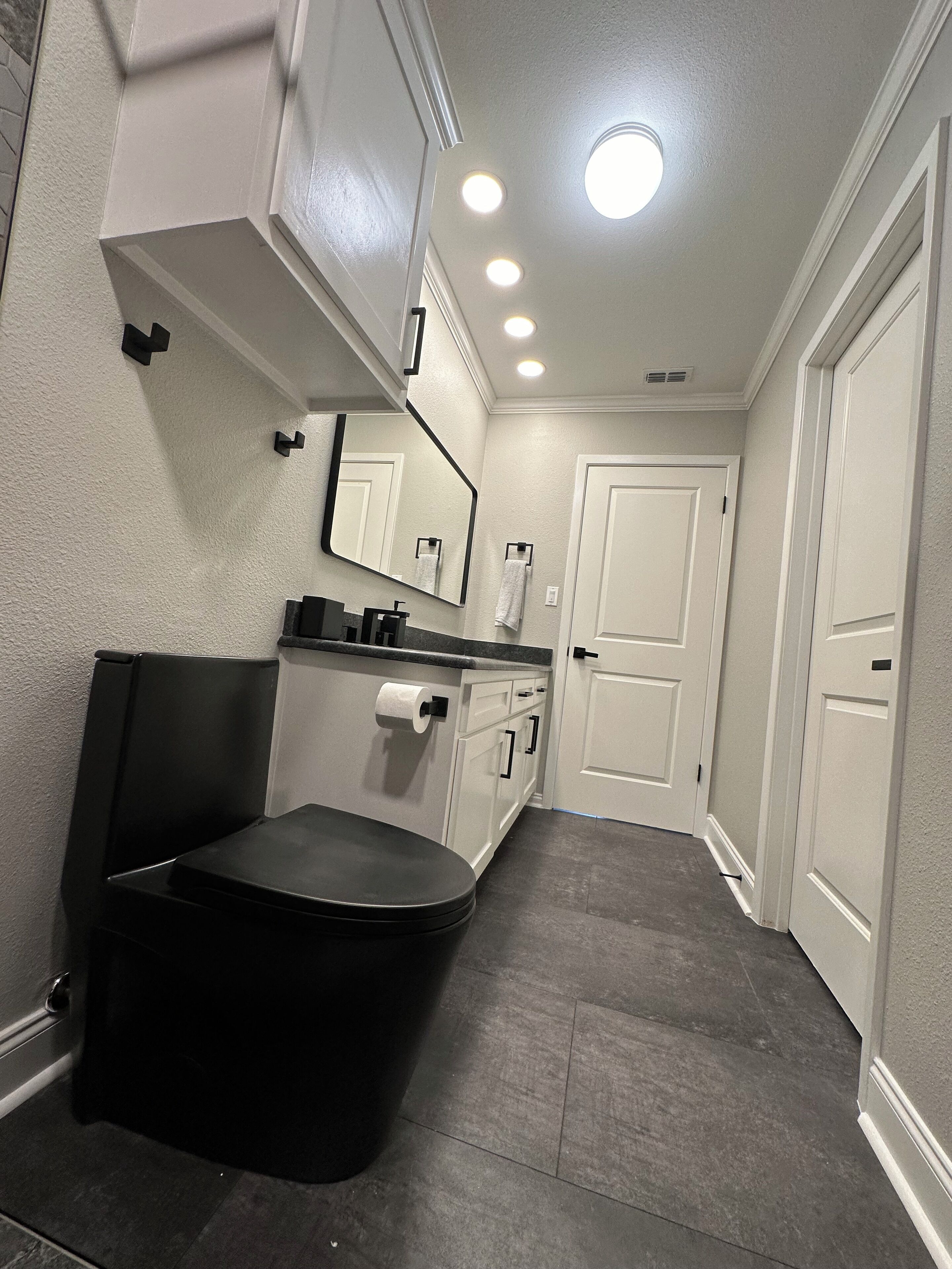 A bathroom with a black vanity, white cabinets, a mirror, and a ceiling light.