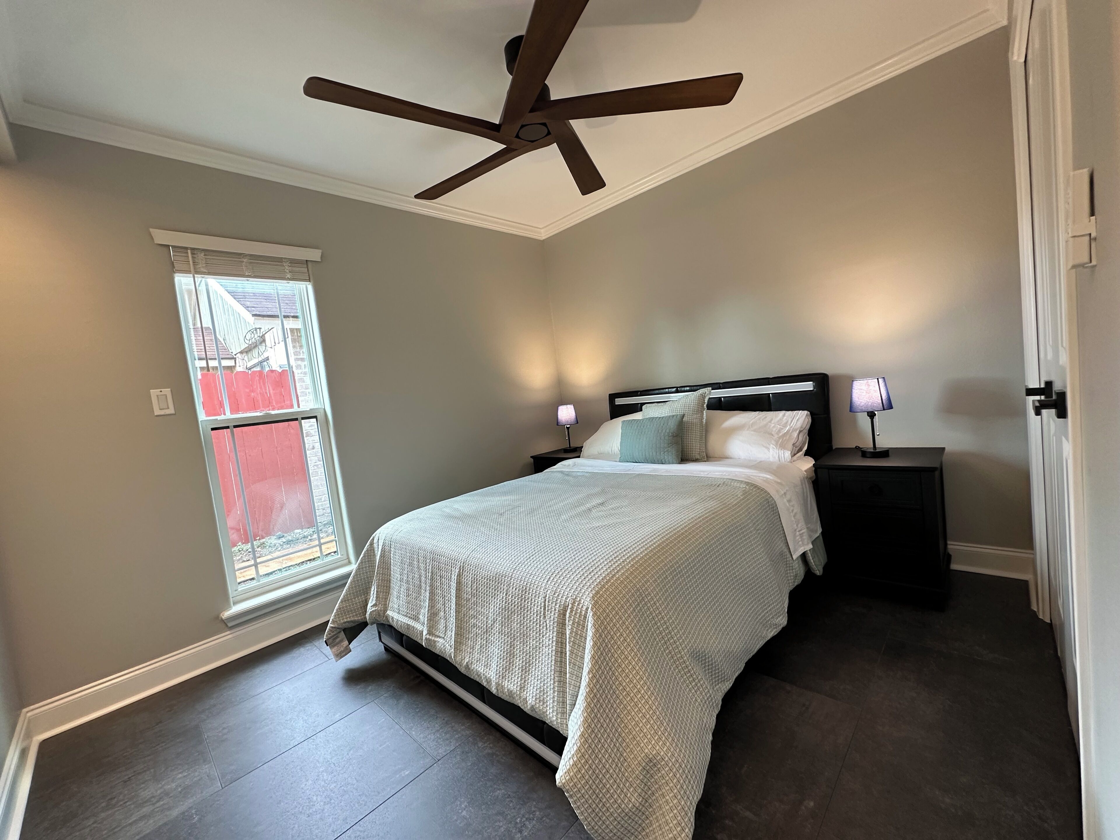 A bedroom with a bed, nightstands, a ceiling fan, and a window with blinds.