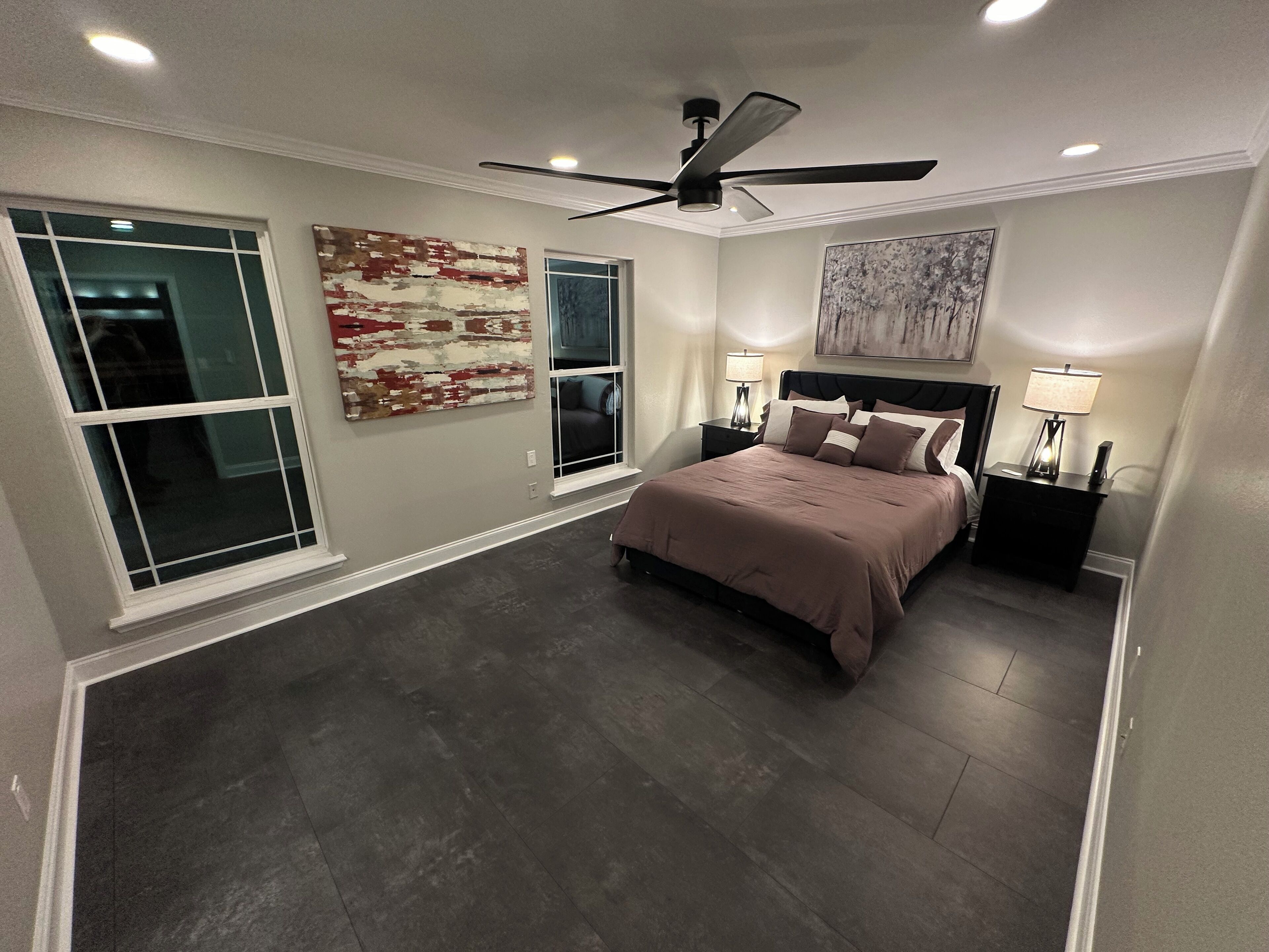 A bedroom with a large bed, two nightstands, a ceiling fan, and artwork on the walls.
