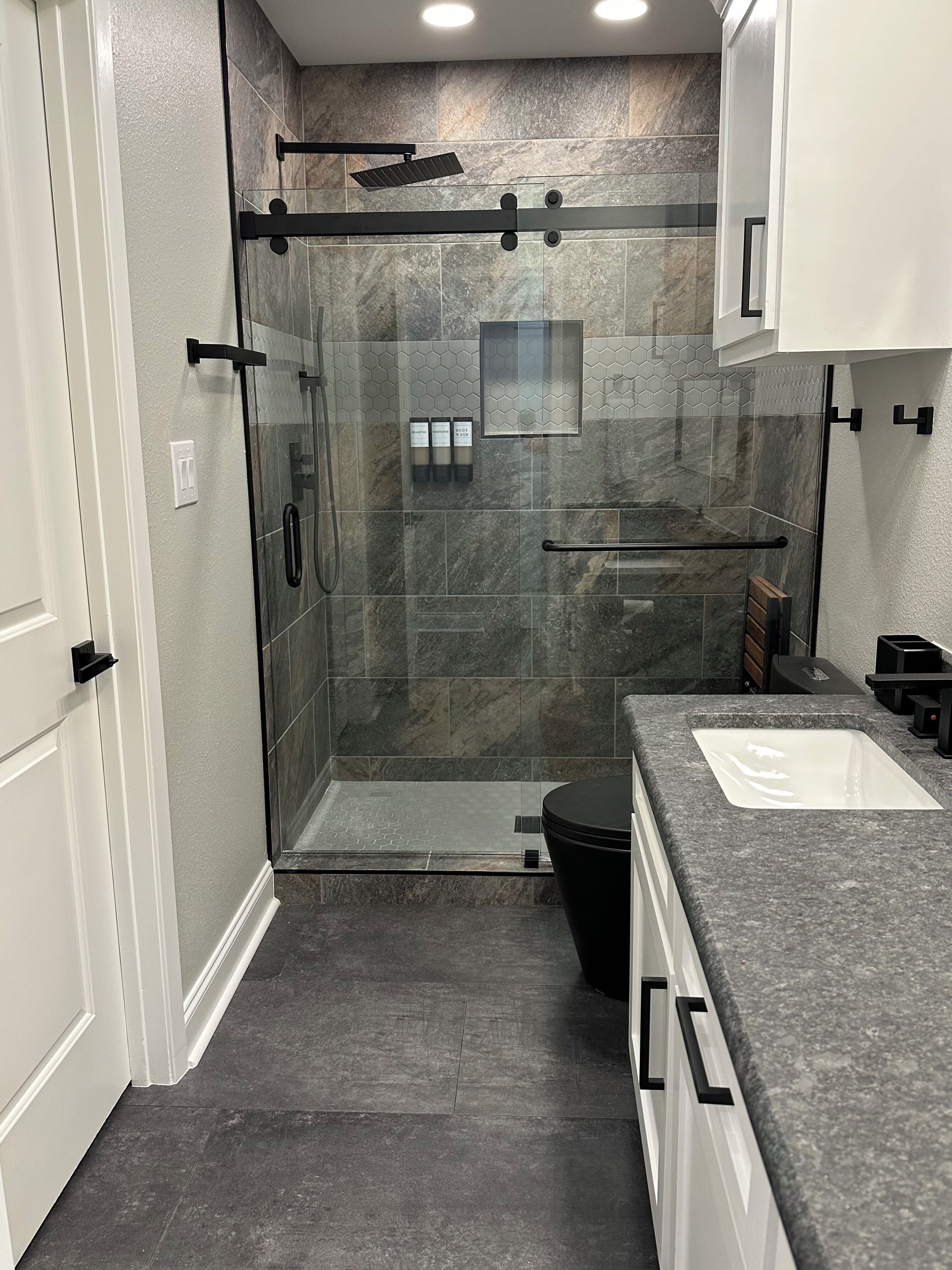Een moderne badkamer met een douche met glazen wand, een wit wastafel en donkere marmeren tegels.