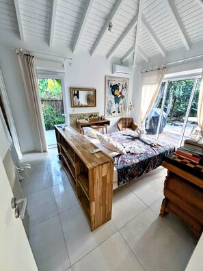 A bedroom with a bed, wooden bench, desk, and a large window.