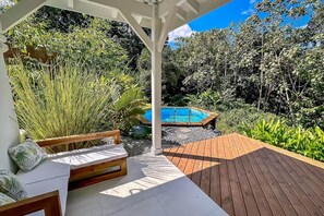 A wooden deck with a pool, surrounded by lush greenery and a wooden bench. - The White Palm - Tropical Villa (Sainte Rose)