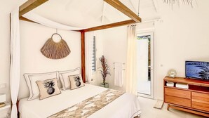 A bedroom with a four-poster bed, a wooden headboard, a bedside table with a TV, and a door leading to a balcony.