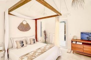 Une chambre à coucher avec un lit à baldaquin, une tête de lit en bois, une table de chevet avec un téléviseur et une porte donnant sur un balcon.