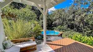 A wooden deck with a pool, surrounded by lush greenery and a wooden bench.