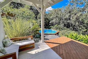 Une terrasse en bois avec une piscine, entourée d’une végétation luxuriante et agrémentée d’un banc en bois.