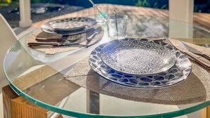 A dining table with a glass top, two blue patterned plates, a clear glass, and a knife on a woven placemat.