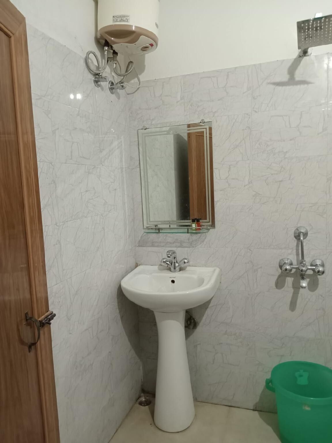 Een badkamer met een witte wastafel, een spiegel, een douchekop en een groene emmer.