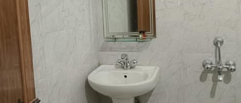 Een badkamer met een witte wastafel, een spiegel, een douchekop en een groene emmer.