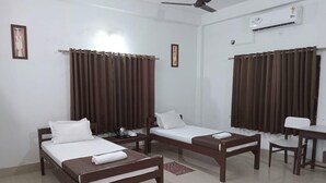 A hotel room with two single beds, a small table, a chair, and a desk. - Sawasstika Eco Park Resort  (Jalpaiguri)