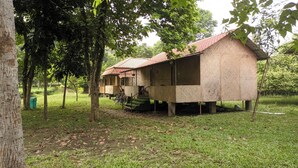A rustic wooden structure with a tiled roof, elevated on stilts, surrounded by trees and grass. - Sawasstika Eco Park Resort  (Jalpaiguri)