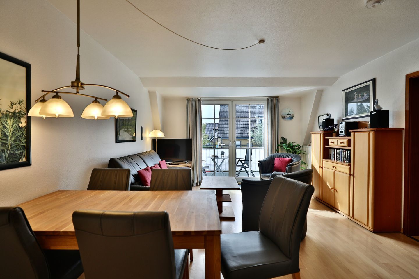 Un salon moderne comprenant une table à manger, des canapés et un téléviseur. Il y a un balcon avec vue sur les immeubles.