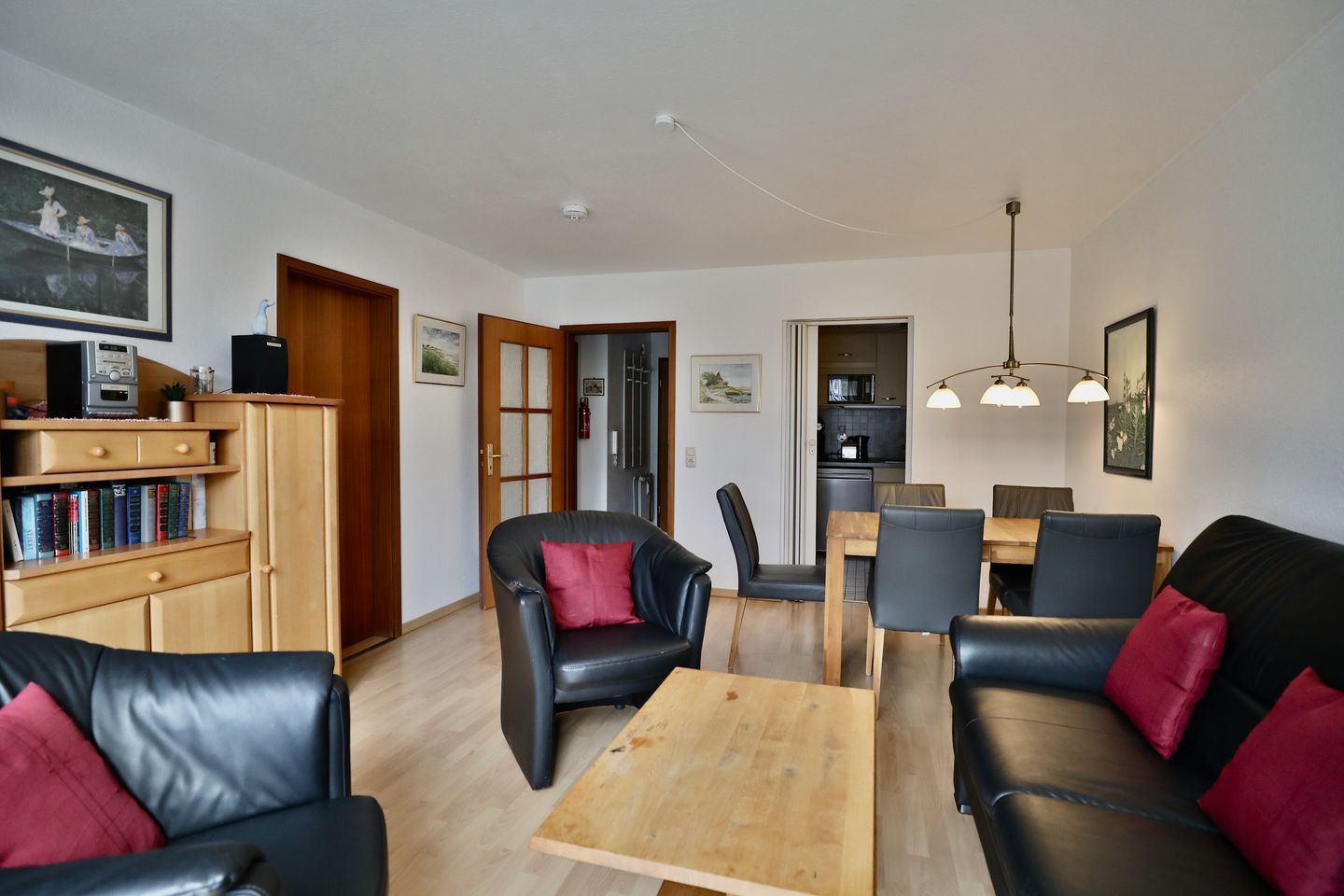 Ein Wohnzimmer mit einer Couch, Sesseln, einem Couchtisch, einem Bücherregal und einem Essbereich mit Tisch und Stühlen.