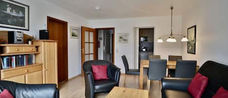 A living room with a sofa, chairs, a coffee table, a bookshelf, and a dining area with a table and chairs.