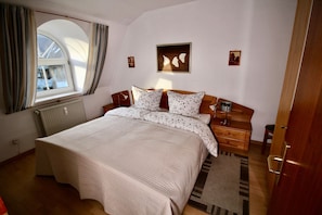 Ein Schlafzimmer mit einem großen Bett, einem Nachttisch, einer Lampe und einem Fenster mit Vorhängen.