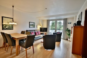 Ein modernes Wohnzimmer mit Essbereich, einer Couch, einem Fernseher und einem Balkon mit Blick.