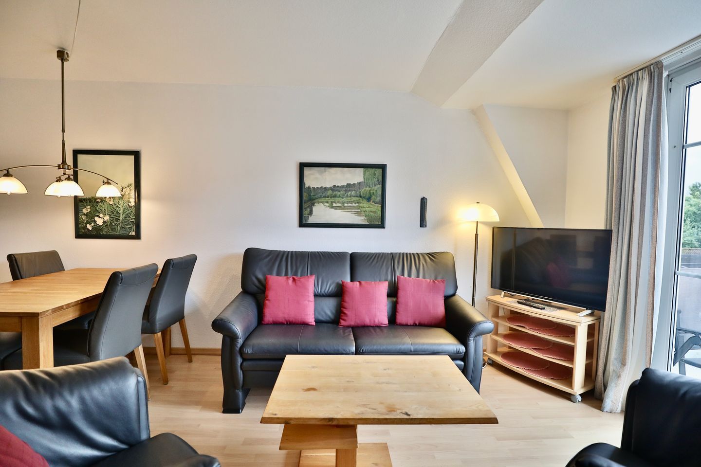 A modern living room with a leather sofa, a wooden coffee table, a dining table with chairs, a flat-screen TV, and a framed landscape painting.