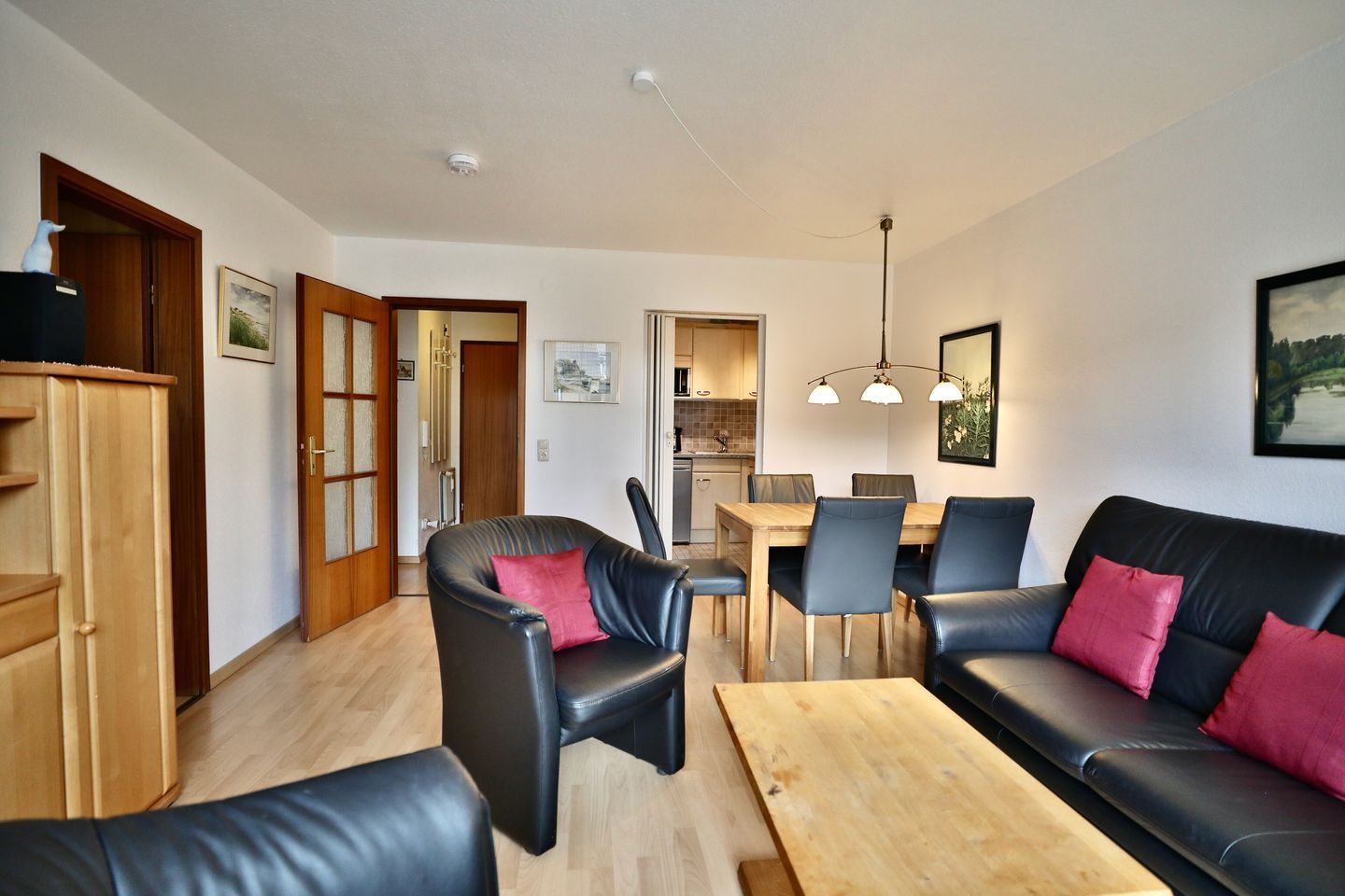A modern living room with a black leather sofa, a wooden coffee table, and a dining area with a wooden table and chairs.