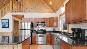A modern kitchen with wooden cabinets, stainless steel appliances, and a wooden ceiling.
