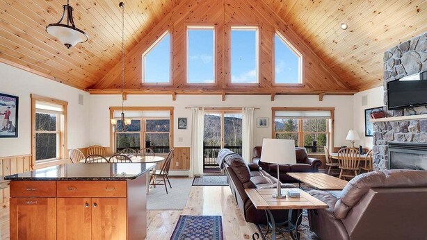 A spacious interior with a high ceiling, wooden beams, a stone fireplace, and a dining area.