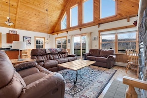 A spacious living area with leather sofas, a wooden coffee table, and large windows offering a view of the outdoors. - Farwell Mountain Retreat (Bethel)