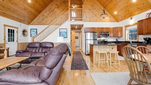 A spacious living area with a leather sofa, wooden flooring, a kitchen with modern appliances, and a staircase leading to an upper level.