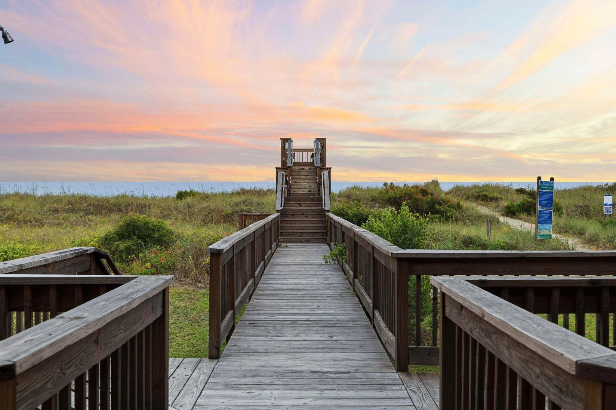 A wooden boardwalk leading to a beach with a sunset in the background.