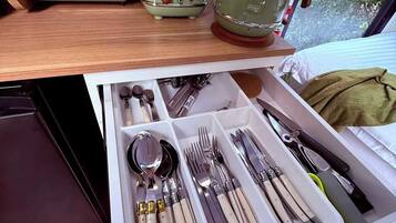 Een lade met netjes geordoneerd bestek en een vintage groene apparatenstel op een houten plank.