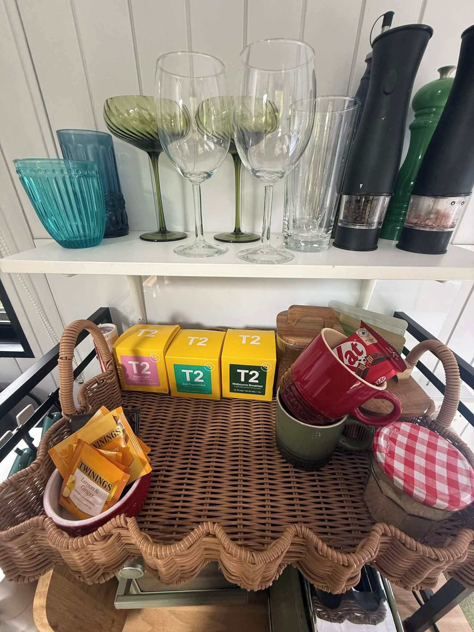 Una cesta de mimbre con artículos de la marca T2, una taza roja y una tapa a cuadros sobre una mesa.
