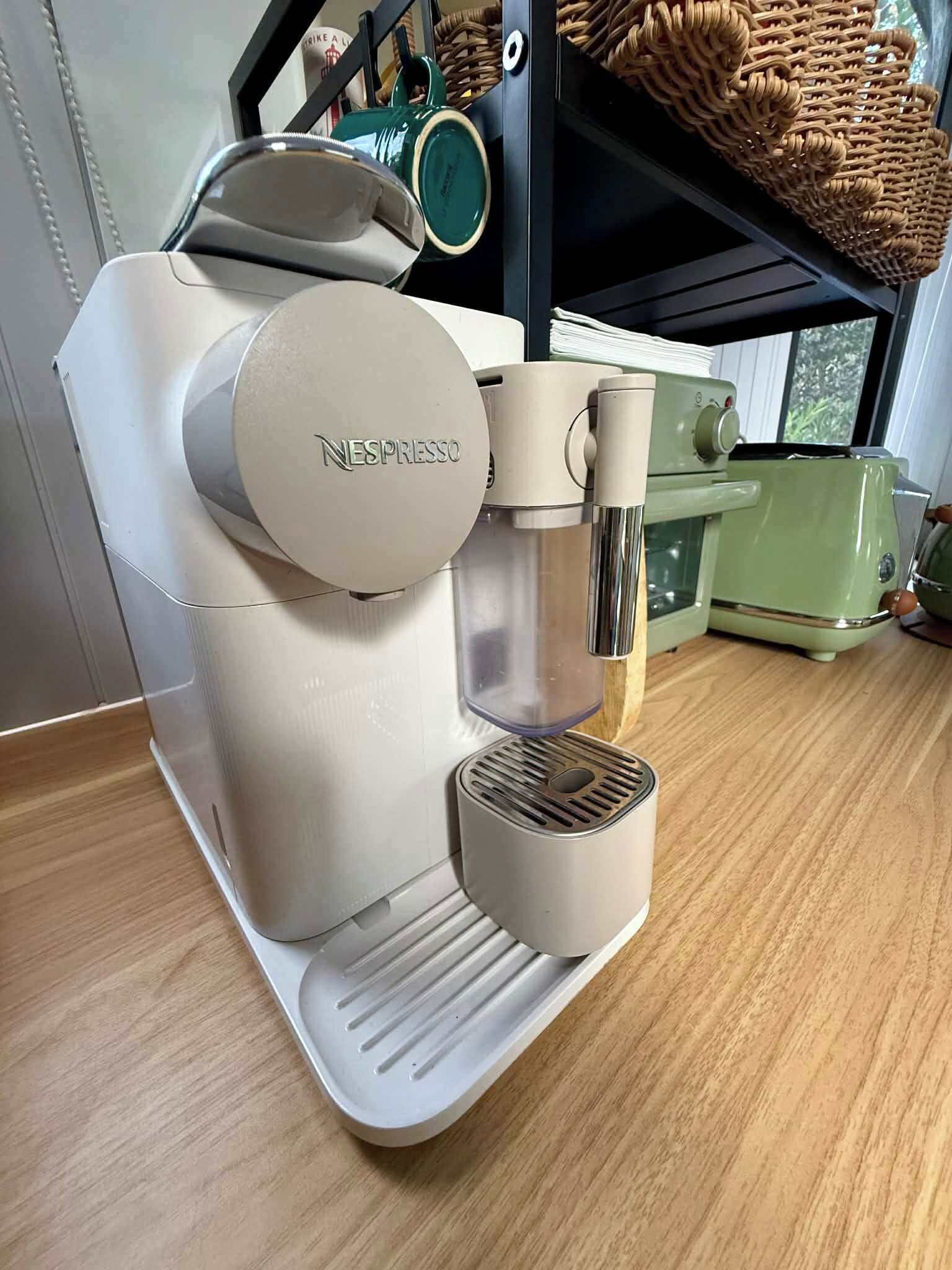 Une machine à café Nespresso posée sur un plan de travail en bois, avec vue sur la fenêtre.