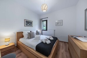 A modern bedroom with a wooden bed, a bedside table with a lamp, a desk with a book, and two framed pictures on the wall. - APARTMENT  CHÂTEL - O Rouge A204 (CHATEL)