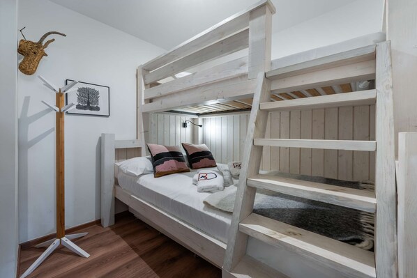 A bunk bed with a white headboard, two pillows, and a blanket. A coat rack with a woven item and a framed picture are on the wall.