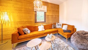 A modern living room with a wooden wall, a sectional sofa, a round coffee table, and a fluffy pouf. - APARTMENT  CHÂTEL - O Rouge A204 (CHATEL)