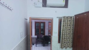 A narrow hallway with a wooden door leading to a room with a bed, a chair, and a small table. - Shree Sitaram Guest House (Faizabad)
