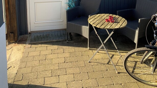 A small outdoor seating area with a table and chairs, a bicycle, and a door with a window.