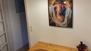 A dining area with a wooden table and two chairs, a painting on the wall, and a hanging light fixture.