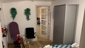 A bedroom with a checkered bedspread, a wardrobe, a desk with a chair, and a small table with a plant.