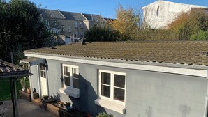A single-story building with a flat roof, a small porch with a bench, and a garden area with potted plants.