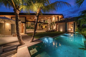 Une maison moderne dotée d’une piscine, d’un espace salon extérieur et de palmiers.