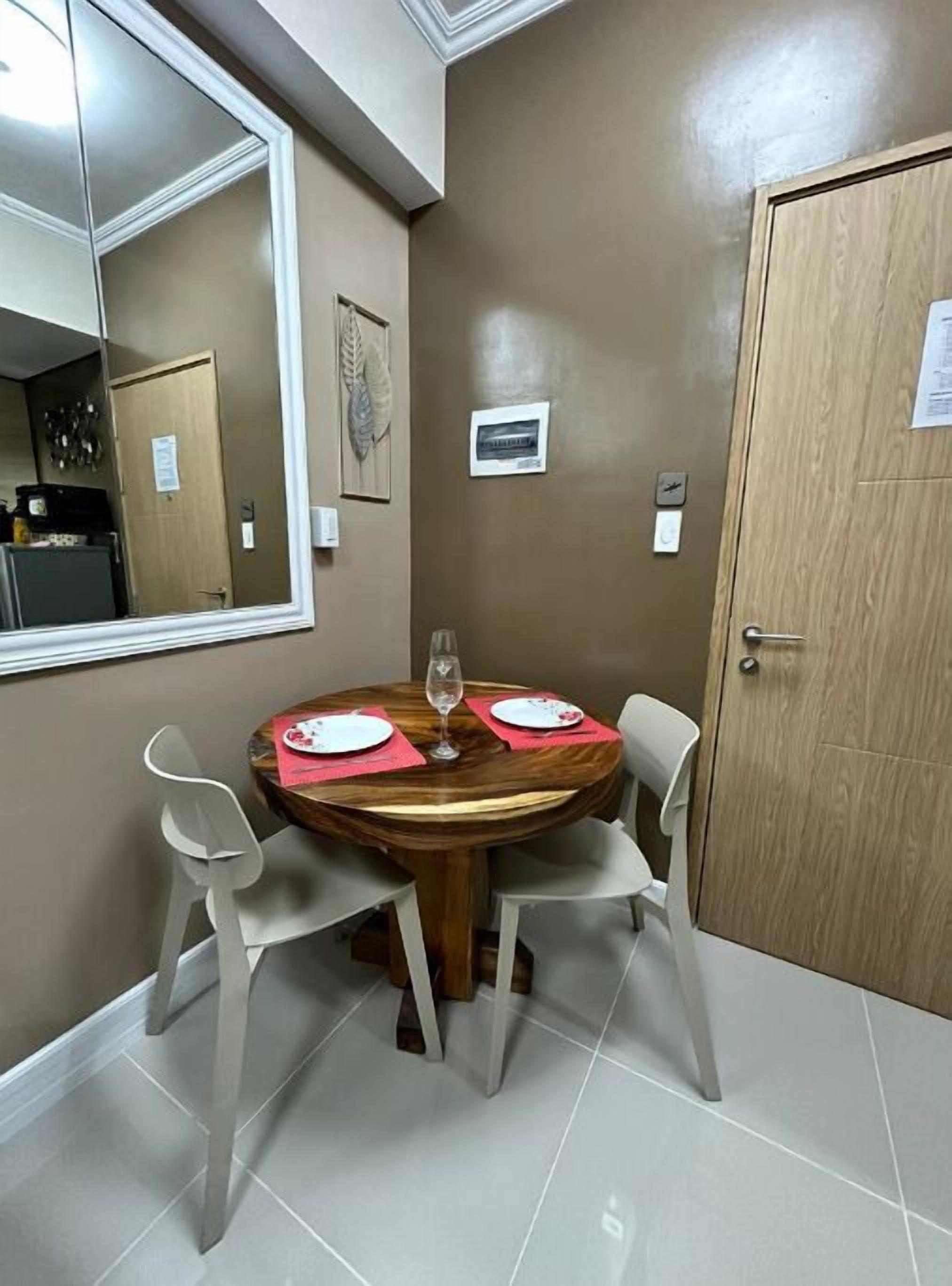 A dining area with a round table, four chairs, a wine glass, and a mirror on the wall.