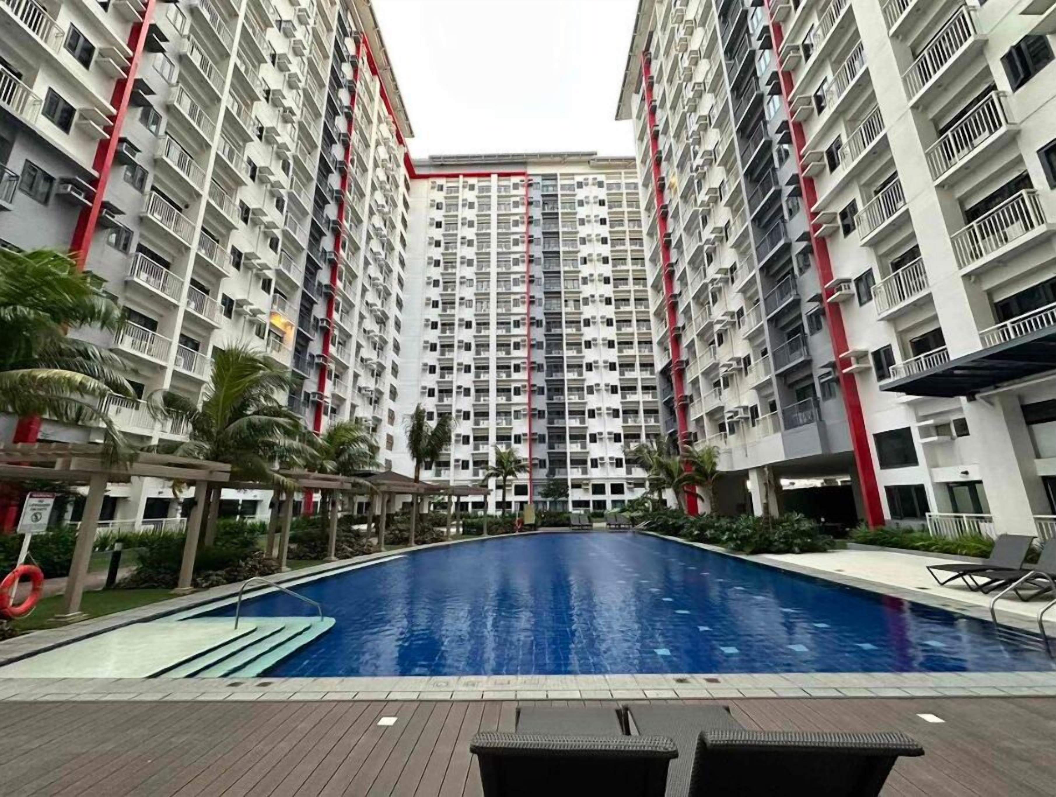A modern residential building with a central swimming pool surrounded by palm trees and lounge chairs.