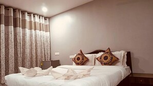 A neatly made bed with patterned pillows, a bedside table, and a curtain with a leaf pattern. - Rainbow Resort Bar and Restaurant (Morjim)