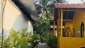 A narrow pathway flanked by lush greenery and buildings with tiled roofs. - Rainbow Resort Bar and Restaurant (Morjim)