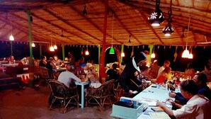 A crowded indoor dining area with tables and chairs, hanging lights, and a concrete counter. - Rainbow Resort Bar and Restaurant (Morjim)