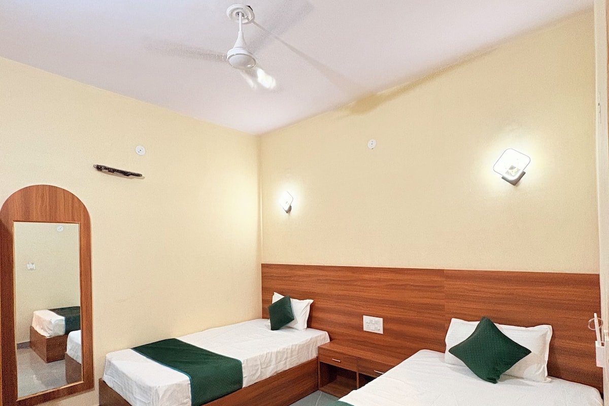 A hotel room with two single beds, a wooden headboard, a ceiling fan, and a mirror on the left wall.