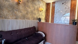 A modern reception area with a dark brown sofa, marble walls, and a ceiling fan. - Jay Ambey Palace (Amer)