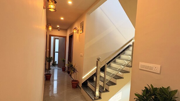 A hallway with a staircase, potted plants, and wall-mounted lighting. - Jay Ambey Palace (Amer)