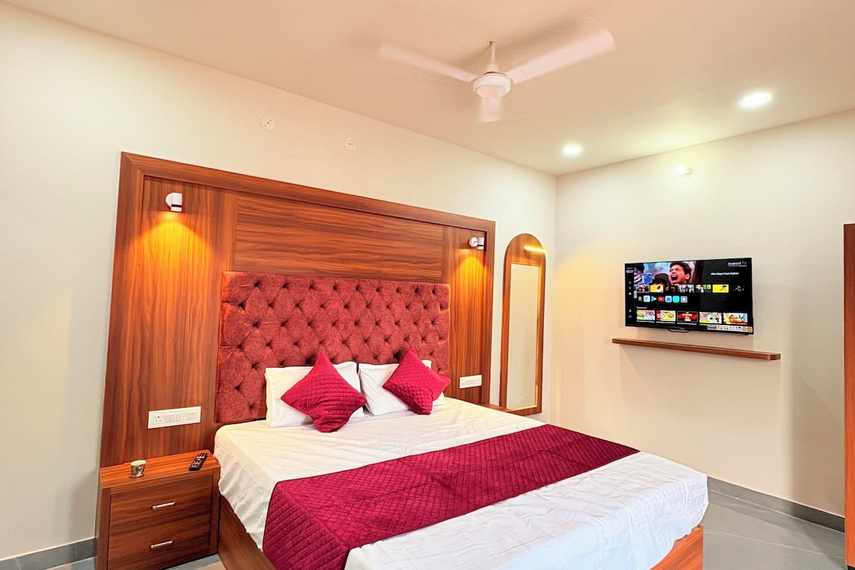 A modern hotel room with a wooden bed frame, a flat-screen TV mounted on the wall, and a ceiling fan.