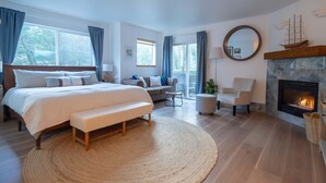 A spacious bedroom with a large bed, a bench, a sofa, a chair, a fireplace, and a view of the outdoors. - Tolovana 3 - 700ft to Beach - Family Fun - Dogs Ok! (Cannon Beach)
